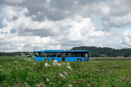 Västtrafiks buss kör på landsväg över blommande fält